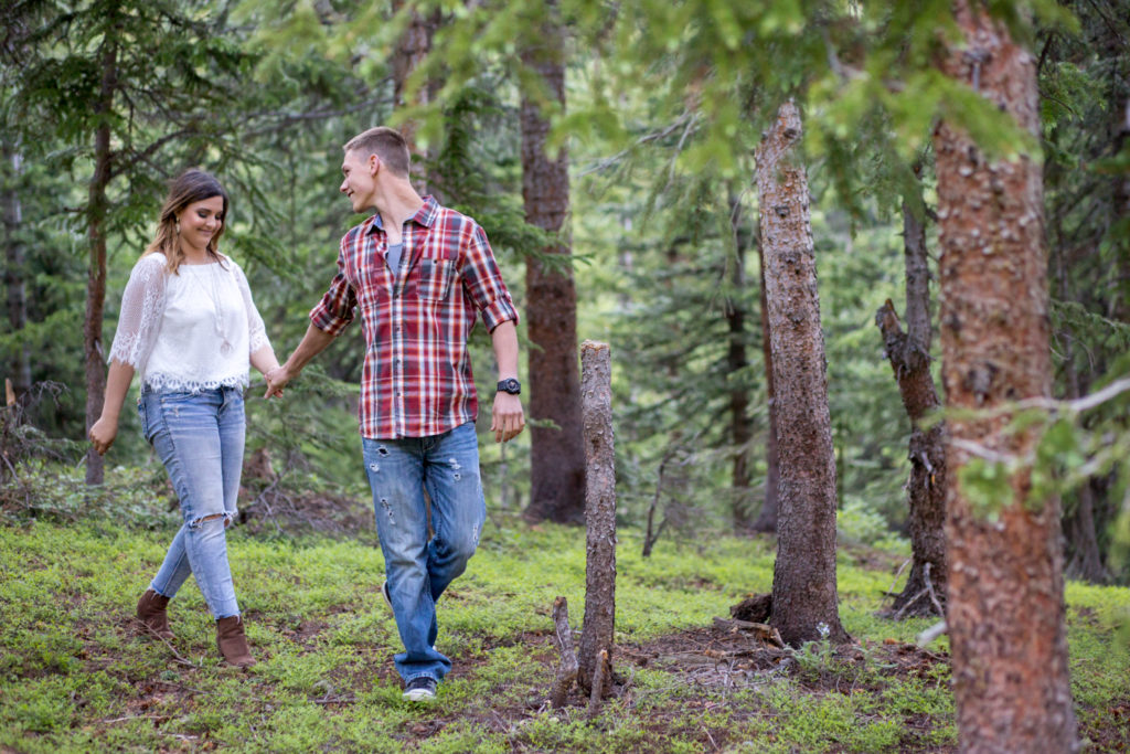loveland pass engagement session colorado couple holds hands and walks in forest guy looks back at his girl