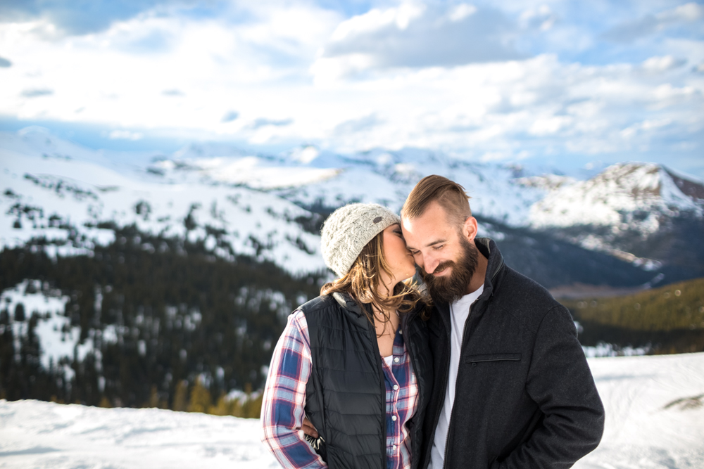 couple wears beanie and plaid for winter snowy loveland pass engagement photo session in Colorado