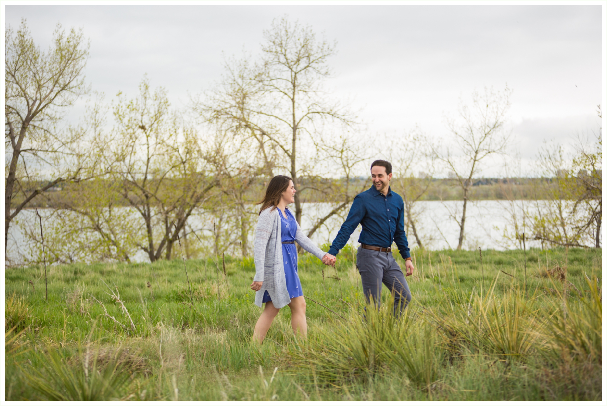 denver engagement photographer shoots spring Colorado session at Cherry Creek Reservoir. Foggy springy engagement session by Colorado engagement photographer Kathryn Kim. couple wears blue and grey engagement outfits and walks along the reservoir, laughing candidly. 